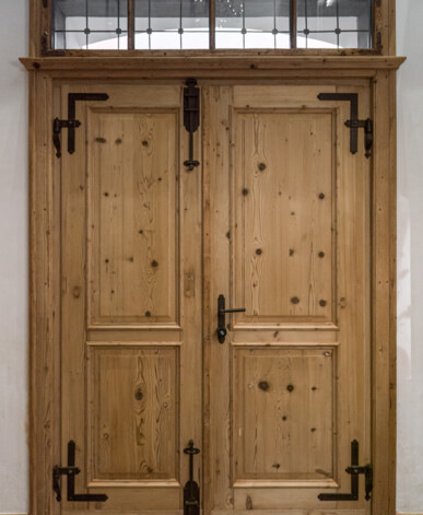Doppeltür aus Altholz mit Oberlicht, sichtbarer Maserung und schmiedeeisernen Beschlägen.