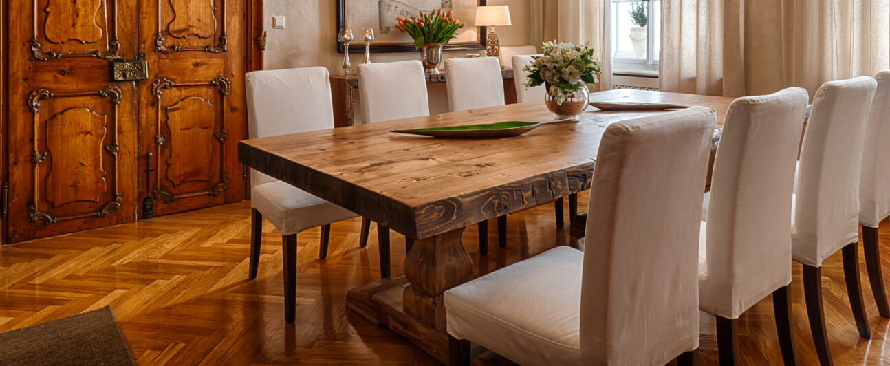 Ein elegantes Esszimmer zeigt Möbel aus Altholz mit Esstisch, Kronleuchter, historischer Holztür und Parkettboden.