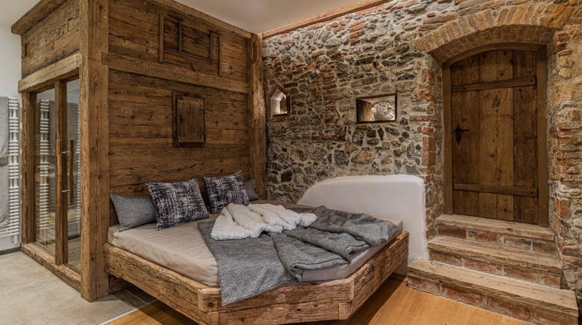 Liegebereich vor einer Sauna aus Altholz vor einer Natursteinwand und einer Holztür.