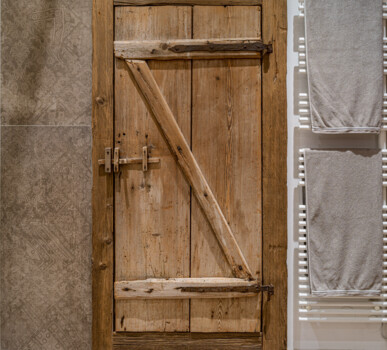 Rustikale Altholz-Badtür mit Z-Verstrebung neben weißem Heizkörper mit grauen Handtüchern.