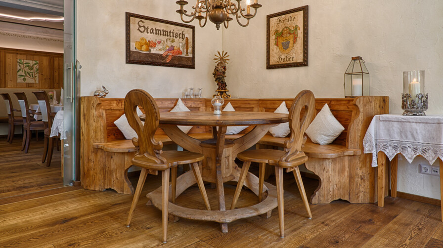 Gemütliche Stube mit runder Eckbank, Tisch und Stühlen, handgefertigten Möbeln aus Altholz, Kronleuchter und Stammtisch-Wandbild.