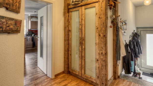 Flur mit maßgefertigtem Schrank aus Altholz und satinierten Glastüren, Garderobe neben Eingang; Blick in Küche im Hintergrund.