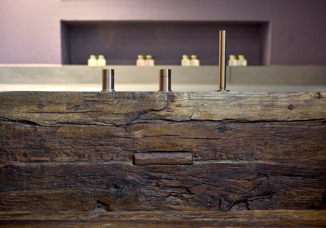 Detail einer massiven Altholz-Front mit modernen Messingarmaturen; rustikale Oberfläche in minimalistischer Umgebung.