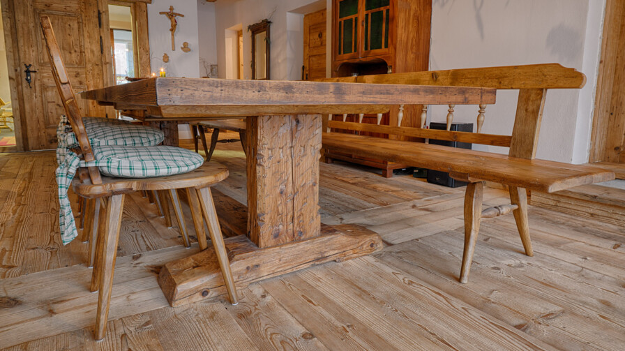 Essbereich mit langer Holztafel, Bank und Stühlen mit Karokissen aus Altholz in traditioneller Stube.