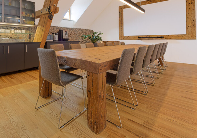 Besprechungsraum mit Möbeln aus Altholz: langer Konferenztisch mit rustikalen Balken, moderne Hängeleuchte, Küchenzeile und Leinwand.