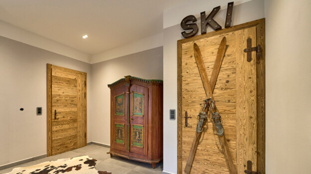 Skikeller mit Altholz-Tür mit alten Skiern darauf. Daneben steht ein bemalter Bauernschrank.