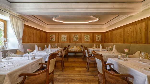 Stilvoller Gastraum mit Holzvertäfelung, weißen Tischtüchern und warmem Licht.