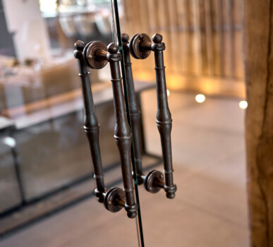 Detailaufnahme patinierter Metall-Türgriffe an einer Glasdrehtür.