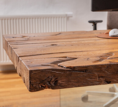 Schreibtischplatte aus Altholz an einem modernen Arbeitsplatz mit Monitor und Mauspad.