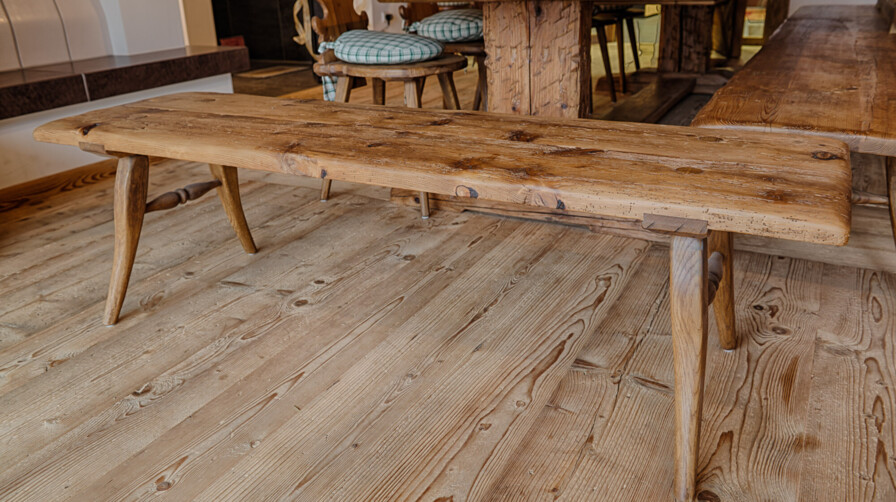 Rustikale Sitzbank aus Altholz mit sichtbarer Maserung in einer Stube, neben passendem Tisch.