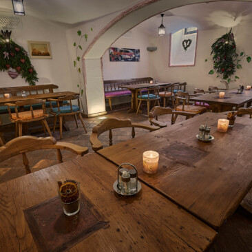 Gemütliche Gaststube mit großen Tischen und Bänken aus Altholz, Kerzenlicht und Deko.