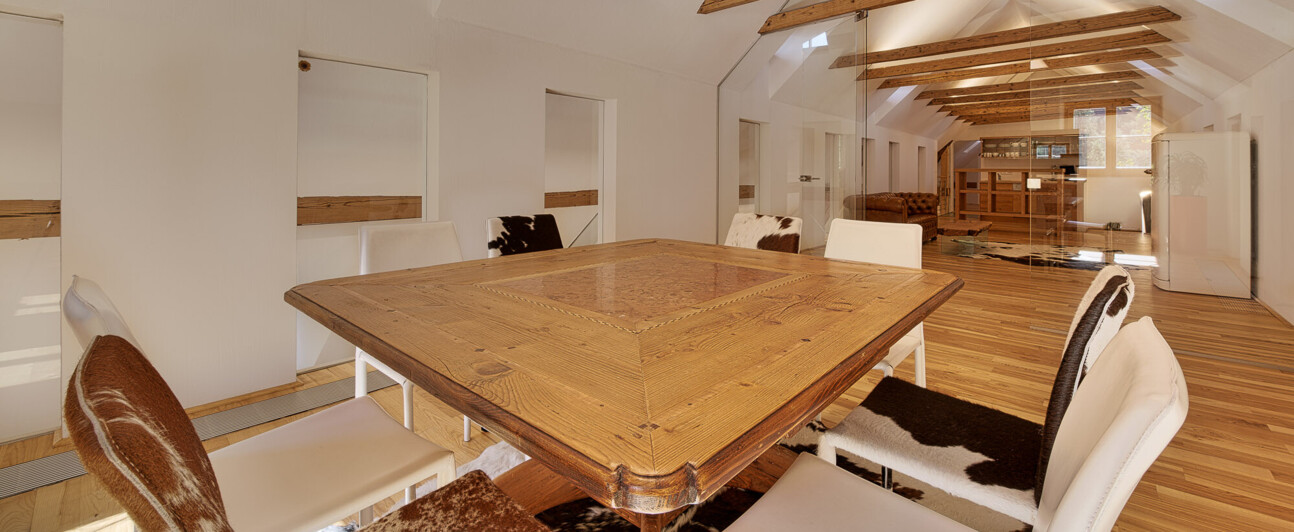 Besprechungsraum mit sichtbaren Holzbalken, massivem Tisch aus Altholz und Stühlen mit Fellbezügen.