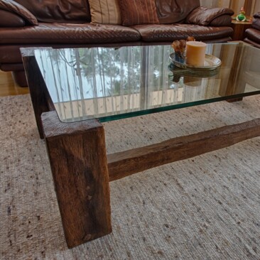 Couchtisch aus Altholz mit Glasplatte, darauf ein Deko-Tablett mit Kerze. Im Hintergrund ein braunes Ledersofa. 