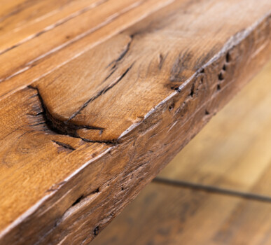 Diese Nahaufnahme zeigt eine Tischkante aus Altholz mit charaktervollen Rissen, typisch für handgefertigte Möbel aus Altholz.
