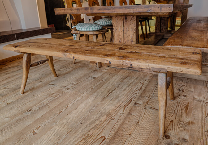 Rustikale Sitzbank aus Altholz mit sichtbarer Maserung in einer Stube, neben passendem Tisch.