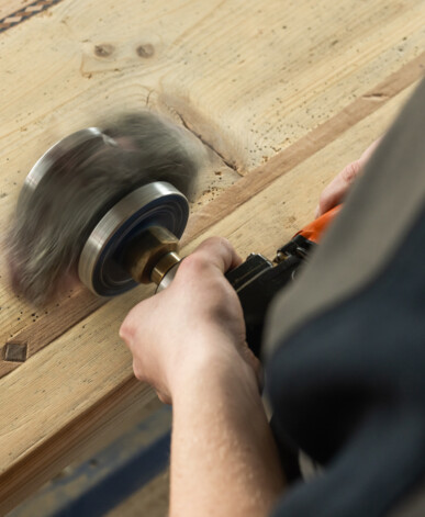 Handwerker bürstet Altholz mit rotierender Bürste, um die Oberfläche zu veredeln und es für Möbel aus Altholz vorzubereiten.