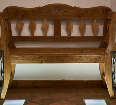 Rustikale Holzbank mit Herzausschnitt und herzförmigen Sprossen, warm beleuchtet auf Terrakottafliesen.