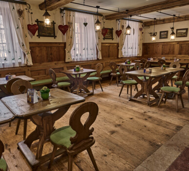 Gemütlicher Gastraum im Alpenstil mit Möbeln aus Altholz: rustikale Tische, Bänke und Stühle, warmes Licht und Herzdeko an den Fenstern.