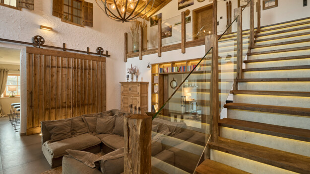 Wohnraum mit Inneneinrichtung aus Altholz, großem Luster, Schiebetür im Scheunenstil und gemütlicher Couch.