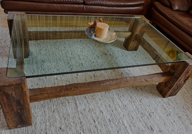 Couchtisch aus Altholz mit Glasplatte, dekoriert mit Kerze auf Teller. Im Hintergrund steht ein braunes Ledersofa.