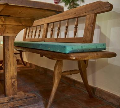 Bank und Tisch aus Altholz mit grünen Sitzpolstern in einer traditionellen Stube.