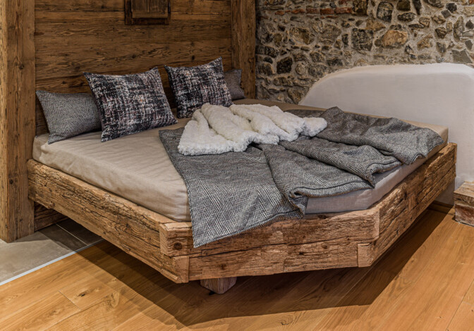 Liegebereich vor einer Sauna aus Altholz vor einer Natursteinwand und einer Holztür.