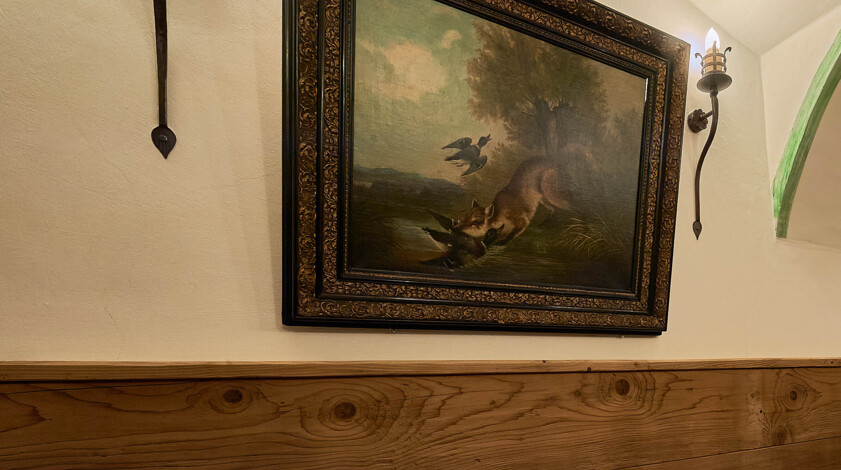 Gemütliche Stube mit Altholzvertäfelung und Holzboden, gewölbter Decke, Wandlampen und Gemälden.