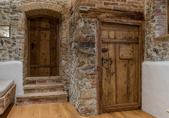 Innenraum mit zwei Altholz-Türen in Natursteinmauer, Ziegelbogen und Stufen, ergänzt von geöltem Holzboden.