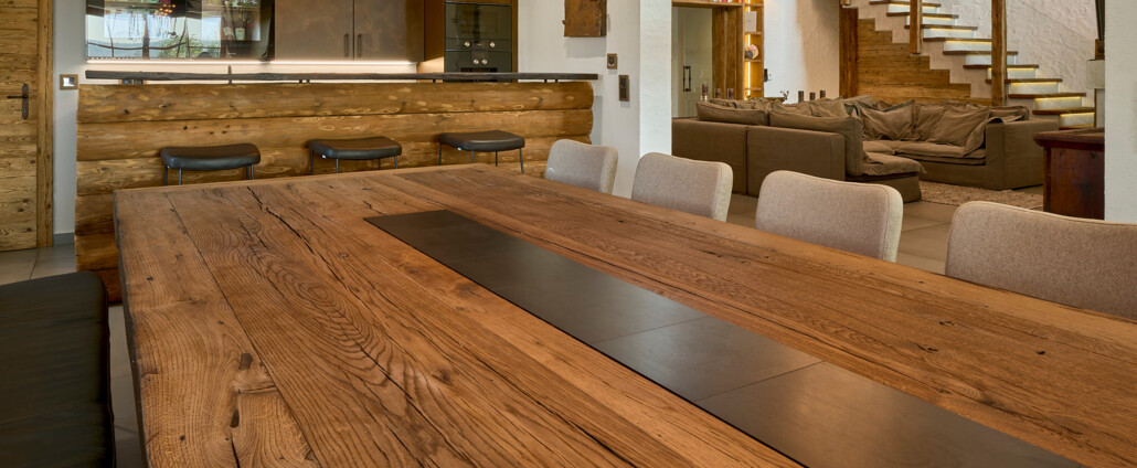 Offener Wohn- und Essbereich mit großem Altholztisch, Hausbar aus Holz, warmen Pendelleuchten und Treppe im Hintergrund.