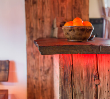 Massive Altholz-Schank mit roter Unterbeleuchtung, darauf eine Holzschale mit Orangen in gemütlicher Atmosphäre.