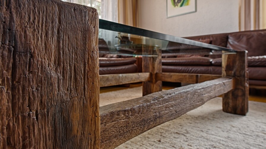 Nahaufnahme eines rustikalen Altholz-Couchtischs mit Glasplatte vor braunen Ledersofas.