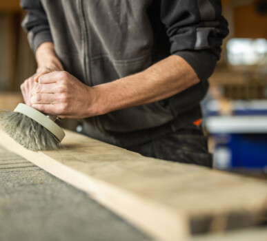 Ein Handwerker bürstet Altholz in der Werkstatt, Vorbereitung für Möbel aus Altholz.