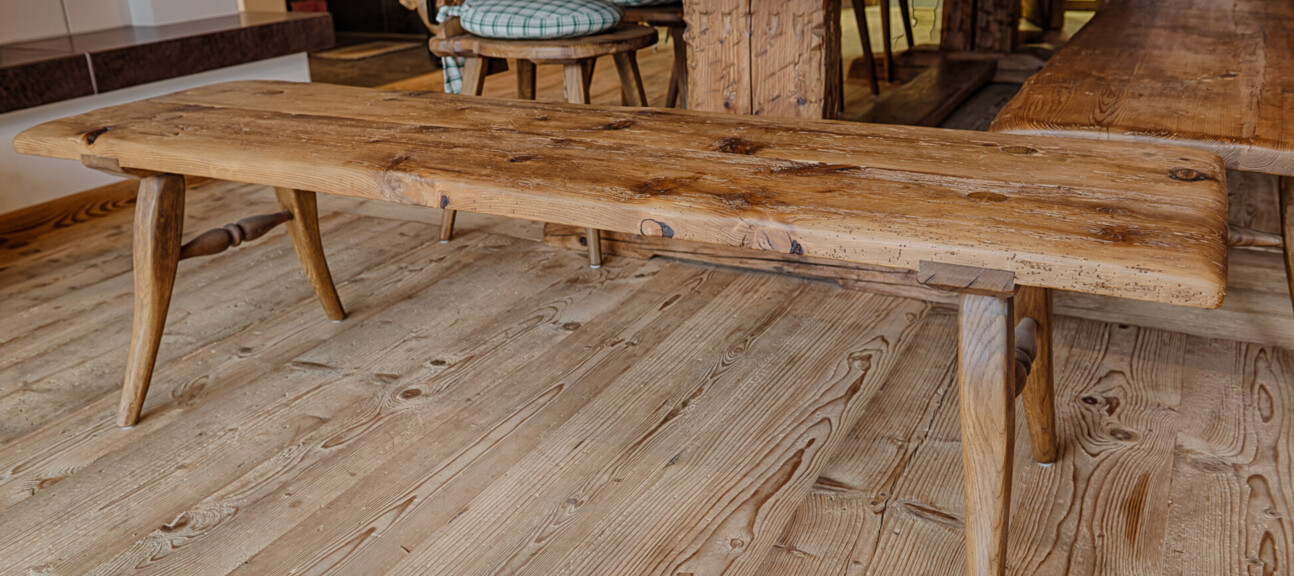 Rustikale Sitzbank aus Altholz mit sichtbarer Maserung in einer Stube, neben passendem Tisch.