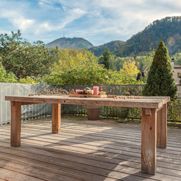 Terrassentisch aus Altholz mit Deko, umgeben von Topfpflanzen und Bergblick.