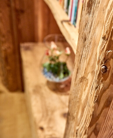 Detail eines Altholz-Regals mit sichtbarer Maserung und Schrauben, im Hintergrund Vase und Bücher.