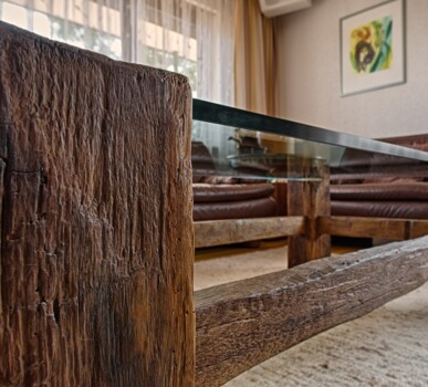 Nahaufnahme eines rustikalen Altholz-Couchtischs mit Glasplatte vor braunen Ledersofas.