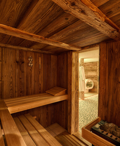 Sauna aus Altholz mit Bänken und Ofen. Blick durch die Tür in den Wellnessbereich.