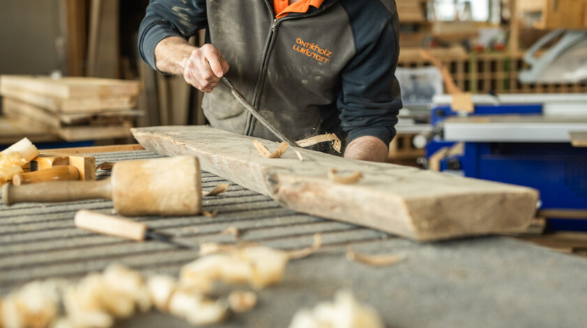Tischler bearbeitet ein Stück Altholz mit einer Hobel für die weiter Verarbeitung für Altholz-Möbelstücke. 
