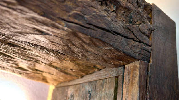 Detailaufnahme eines rustikalen Altholz-Türsturzes mit tiefen Rissen und Patina.