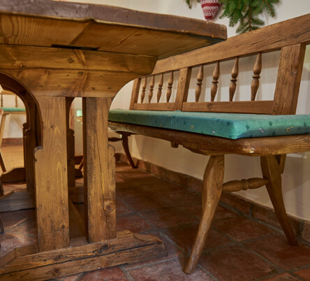 Bank und Tisch aus Altholz mit grünen Sitzpolstern in einer traditionellen Stube.