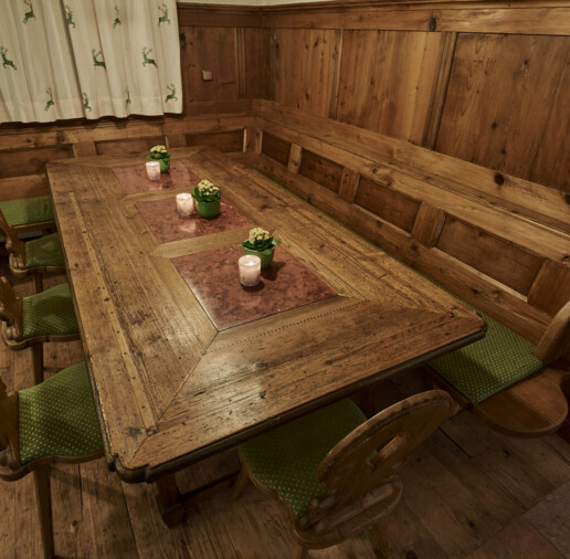 Stube mit Eckbank und Tisch aus Altholz mit grünen Sitzpolstern, Kerzen und kleinen Pflanzen.