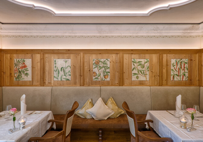 Gemütliche Stube mit Holzvertäfelung, botanischen Paneelen und weiß gedeckten Tischen.