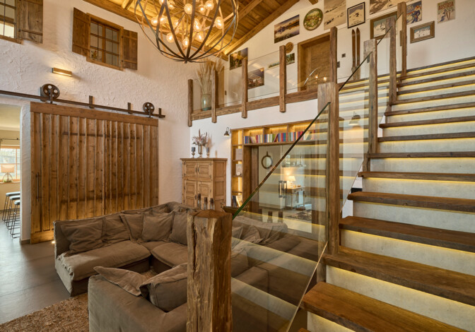 Wohnraum mit Inneneinrichtung aus Altholz, großem Luster, Schiebetür im Scheunenstil und gemütlicher Couch.
