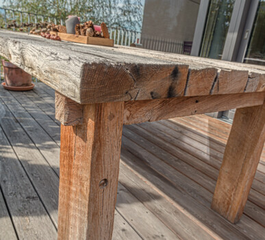 Massiver Tisch aus Altholz auf einer Terrasse, mit rustikaler, rissiger Tischplatte und naturbelassener Patina.