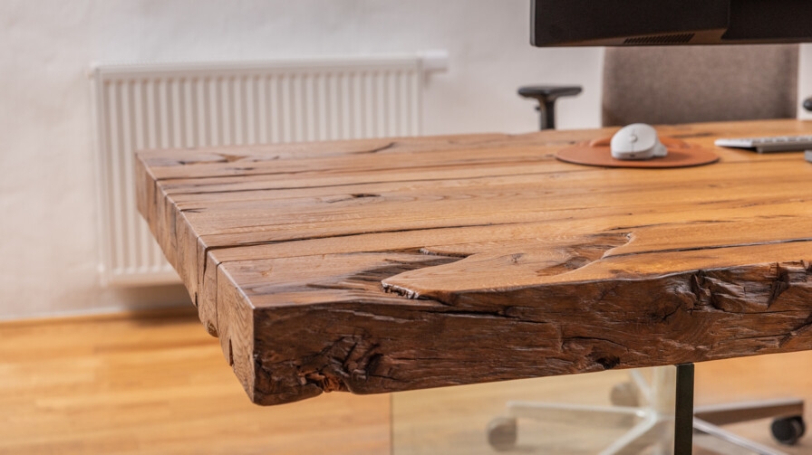 Schreibtischplatte aus Altholz an einem modernen Arbeitsplatz mit Monitor und Mauspad.