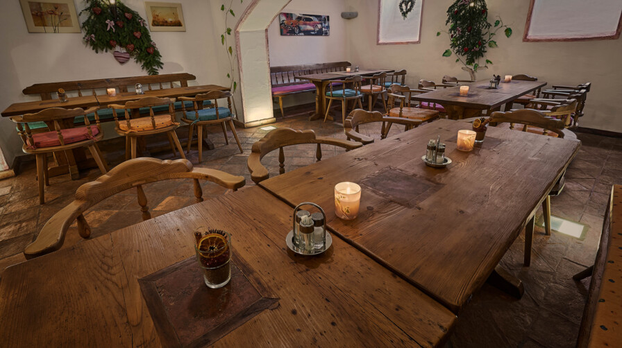 Gemütliche Gaststube mit großen Tischen und Bänken aus Altholz, Kerzenlicht und Deko.