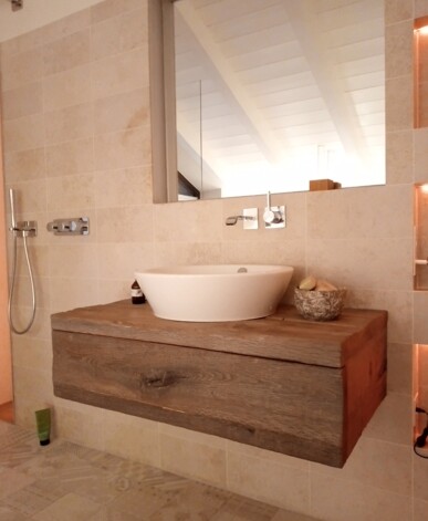 Schwebender Waschtisch aus Altholz mit ovalem, weißem Aufsatzwaschbecken, Wandarmatur und großem Spiegel in einem hellen Bad.