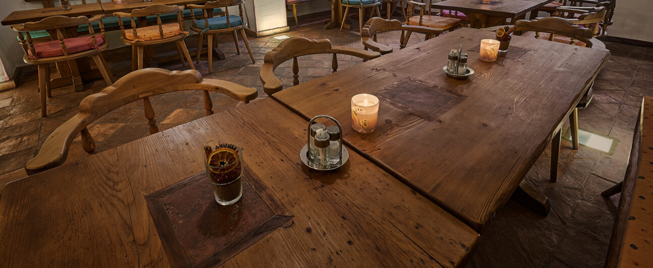 Gemütliche Gaststube mit großen Tischen und Bänken aus Altholz, Kerzenlicht und Deko.