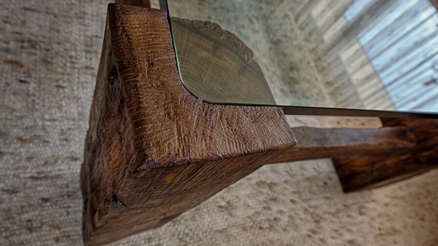 Detail eines handgefertigten Altholz-Tisches mit präzise eingelassener Glasplatte und rustikaler Oberfläche.