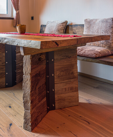 Maßgefertigter Esstisch mit Eckbank aus Altholz, rustikale Oberfläche und Metallbeschläge, mit Kissen in einer gemütlichen Stube.